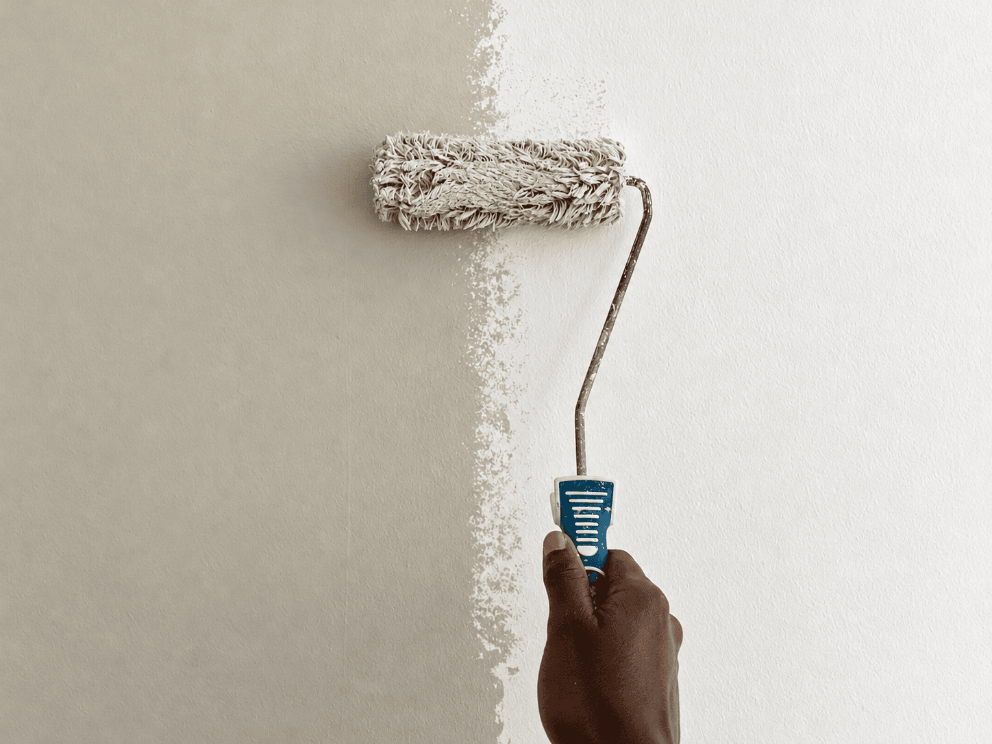 A hand applying paint to an interior wall with a roller